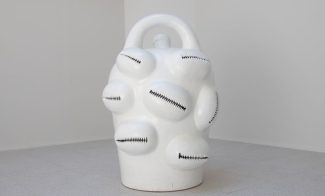 A large white sculpture of a jug with cowrie shells.