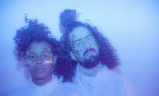 The two members of Optic Bloom with stars on their faces in a blue colored photograph.