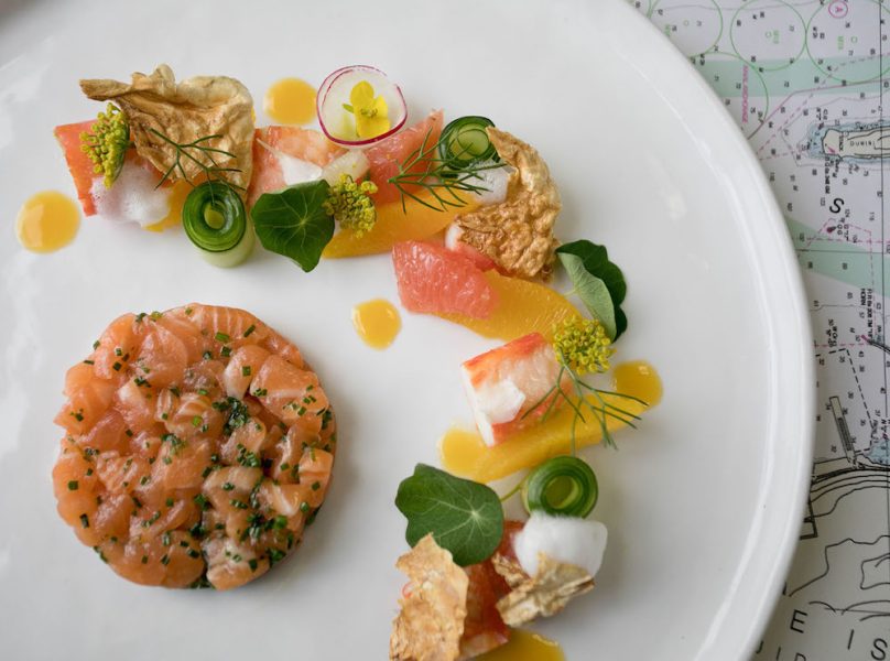 A dish with raw salmon, citrus, and herbs on a white plate