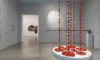 Gallery with circular white drawing on wall and red stringed installation hanging from ceiling