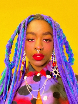 Headshot of person with long purple and teal braids and red makeup against a solid yellow background