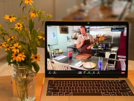 A laptop showing a chef in a profession kitchen sits next to a jar of cut flowers.