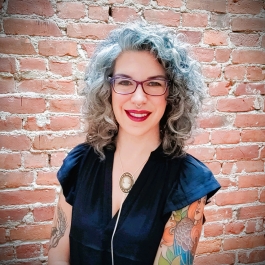Photo headshot of tattooed person with curly silver hair