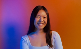 Headshot of a woman with long black hair smiling against a colorful gradient background