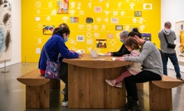 A group of visitors of varying ages draw together at a table in the galleries