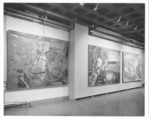 Black and white photo of installation view of Matta: showing three large rectangular paintings with elaborate lines and figures against a wall.