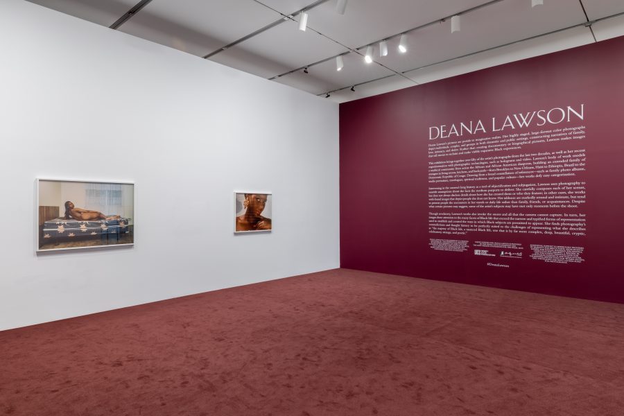 Two framed photos of Black women hang on a white wall opposite a painted burgundy wall with white text and 