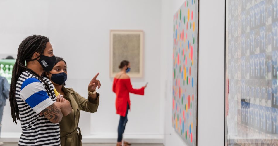 Two visitors viewing an artwork on a wall and one of them pointing at it.