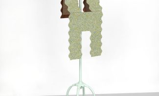 A sculpture of a scalloped form of speckled gold and green linoleum resembling a vest, draped over a dressmaker's work stand.