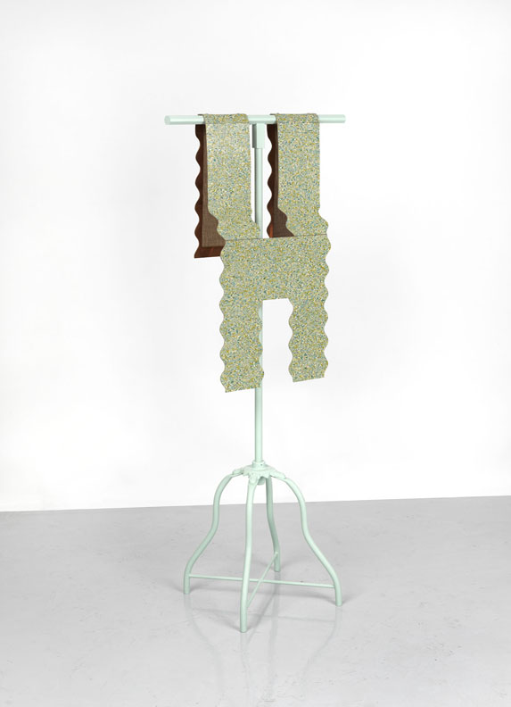 A sculpture of a scalloped form of speckled gold and green linoleum resembling a vest, draped over a dressmaker's work stand.
