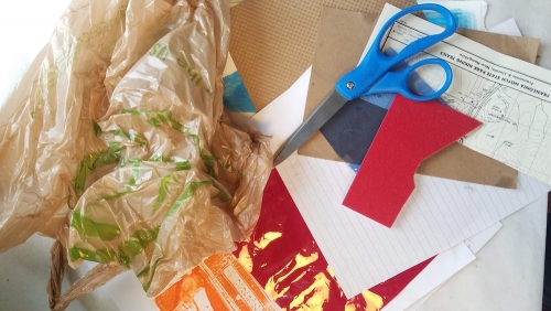 Art making supplies including scissors, an assortment of scrap paper and a brown plastic bag.