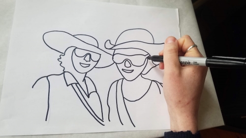 A hand with a sharpie marker over a line drawing of two smiling figures.