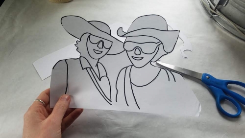 A hand holding up a cut-out silhouette of a line drawing of two smiling figures.
