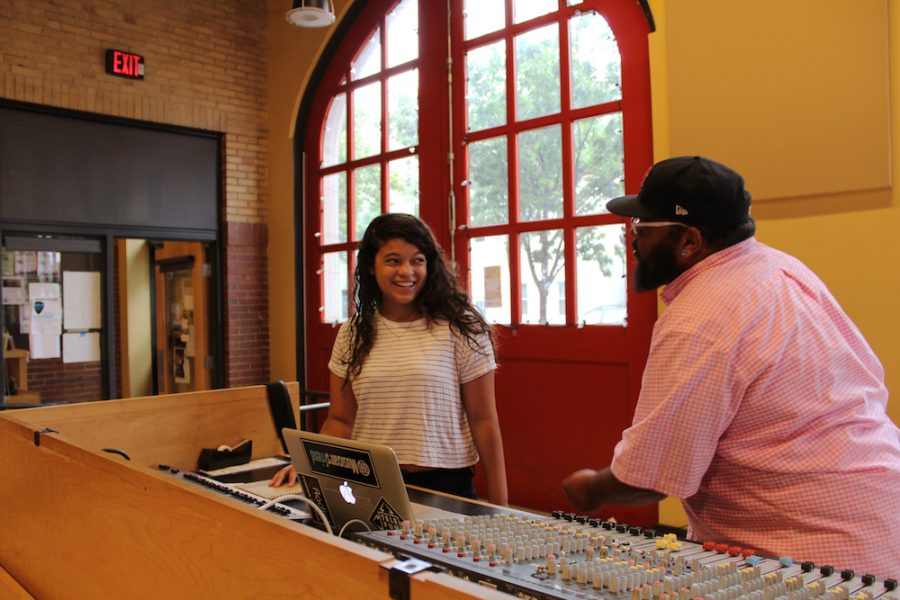 A young woman and a man smile at each other behind a sound mixing board.