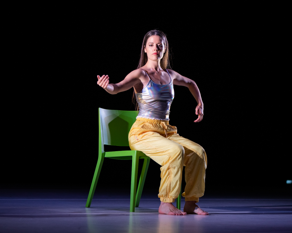 A dancer performing on a stage, seated on a chair