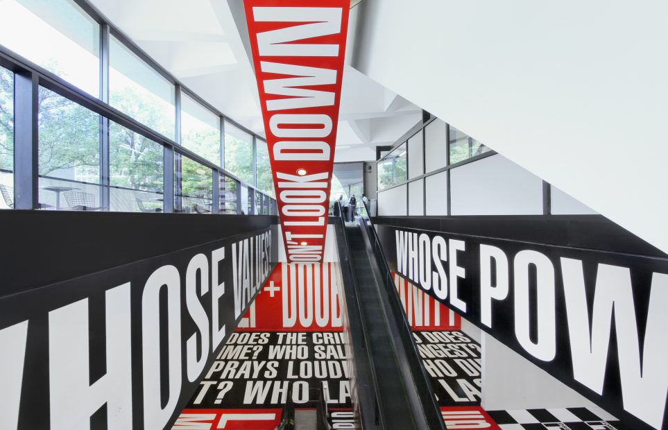 Installation utilizing white text on red and black backgrounds surrounding escalator
