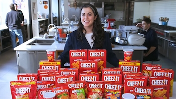 A woman standing behind dozens of boxes of Cheez-Its in a large commercial kitchen