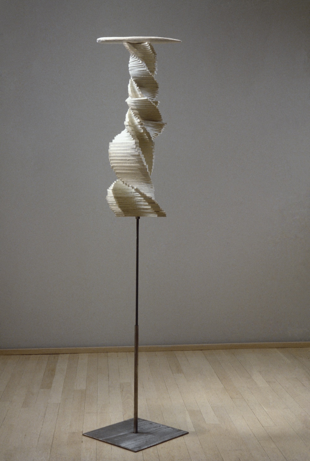 A wooden sculpture of a spiraling form atop a steel rod.  