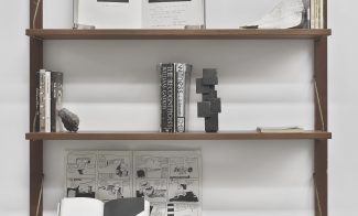 A sculptural installation of books, a bronze sculpture, a rock, and other objects displayed on three wooden shelves.