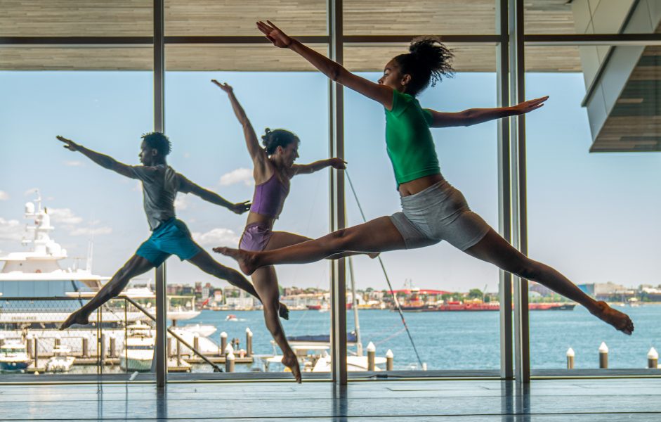Three dancers leaping in the ICA's theater with a view of Boston Harbor.