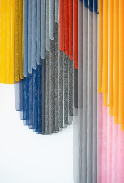 A close-up view of vibrant and colorful bands of coated mesh fabric hung and draped at various lengths. 