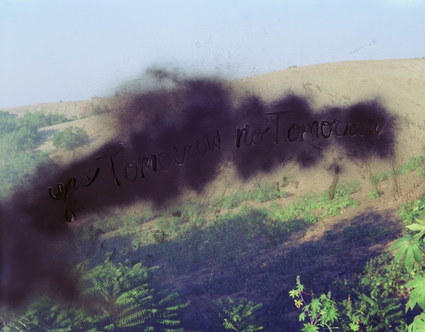 A color photograph of a sandy dune with plants obscured by a cloudy, black form with the words 