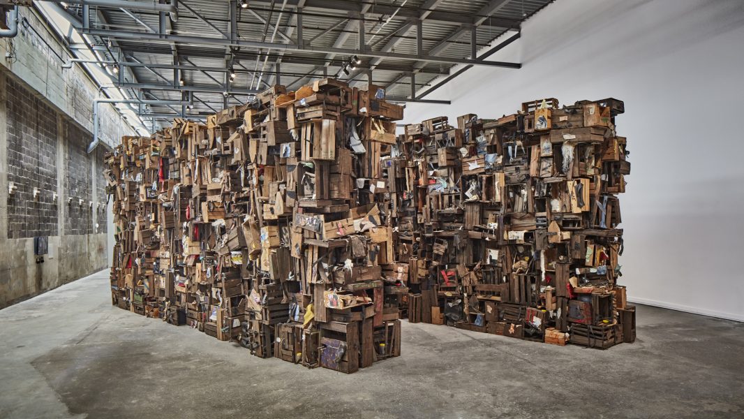 Two walls of wooden crates and debris installed in a warehouse gallery