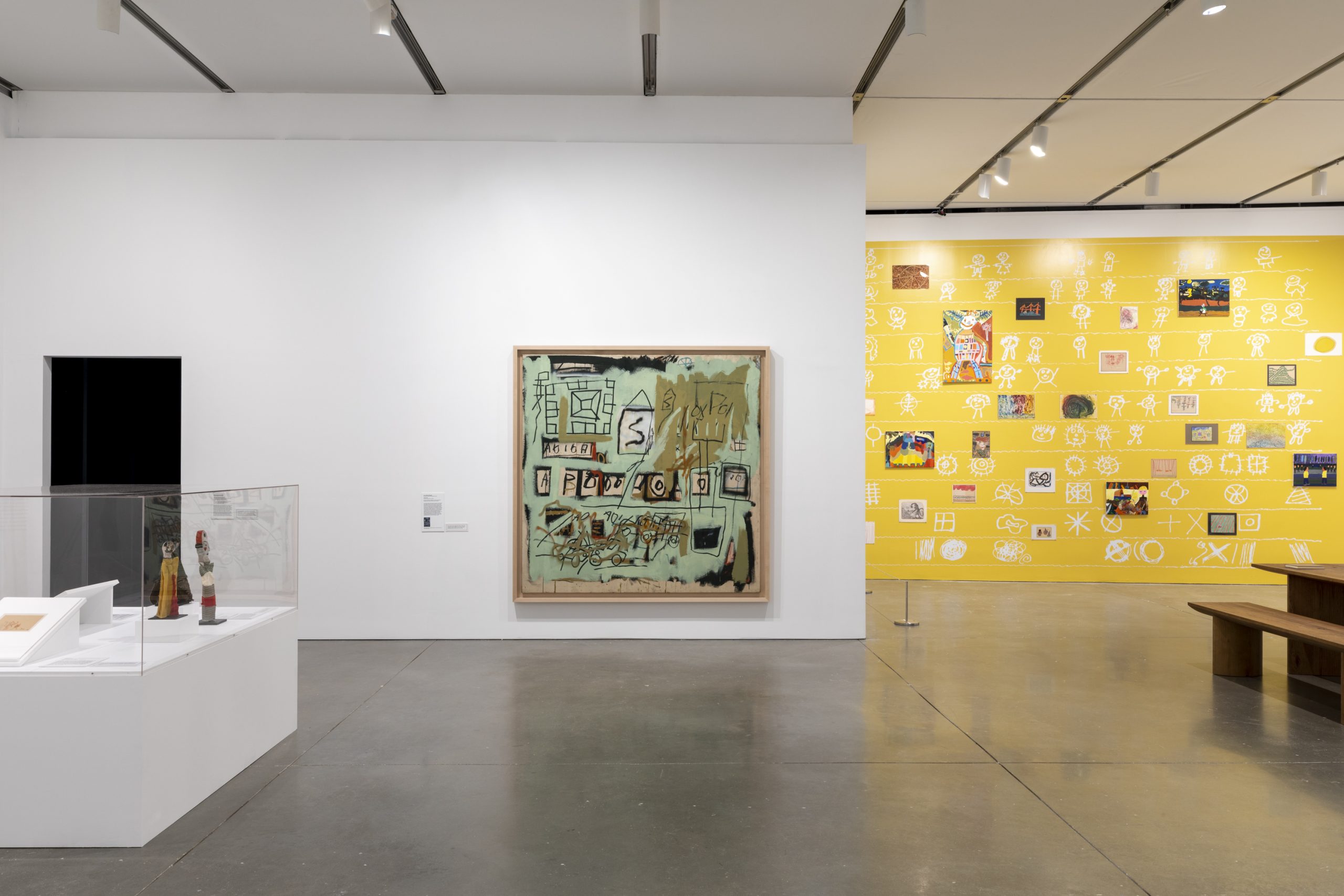 A gallery with a green abstract painting in the middle, a glass case with objects, and a yellow wall to the right