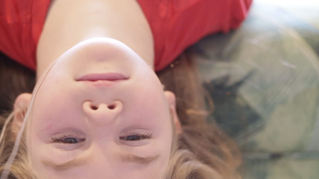 A downward perspective of a young person with the head oriented upside down looking at the camera.