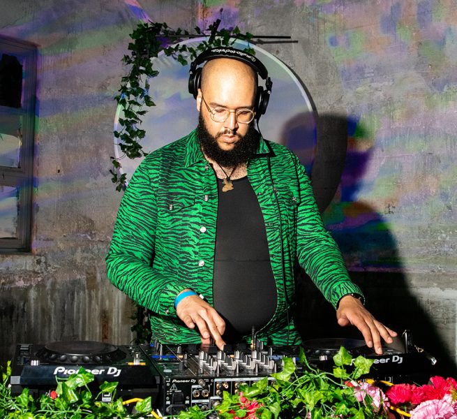 A DJ dressed in a green jacket plays a set