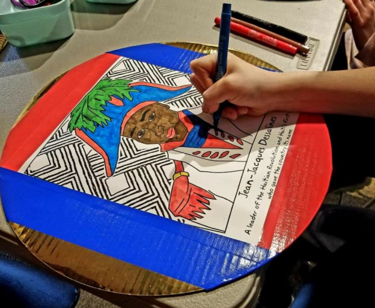 A hand holding a marker coloring in a portrait of Jean-Jacques Dessalines, an African-American figure wearing an 18th-century French-style army uniform.