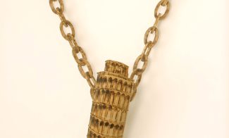 A sculpture made of carved wood and painted to appear like a miniature Tower of Pisa souvenir dangling from a chain necklace.