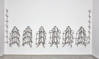 An installation of a row of six rope nets hanging on a wall, with two longer lengths of rope hanging vertically on either side.
