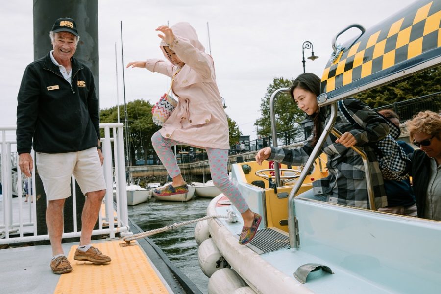 A kid jumping onto the dock from a water taxi while their parent also exits the water taxi and an attendant looks on