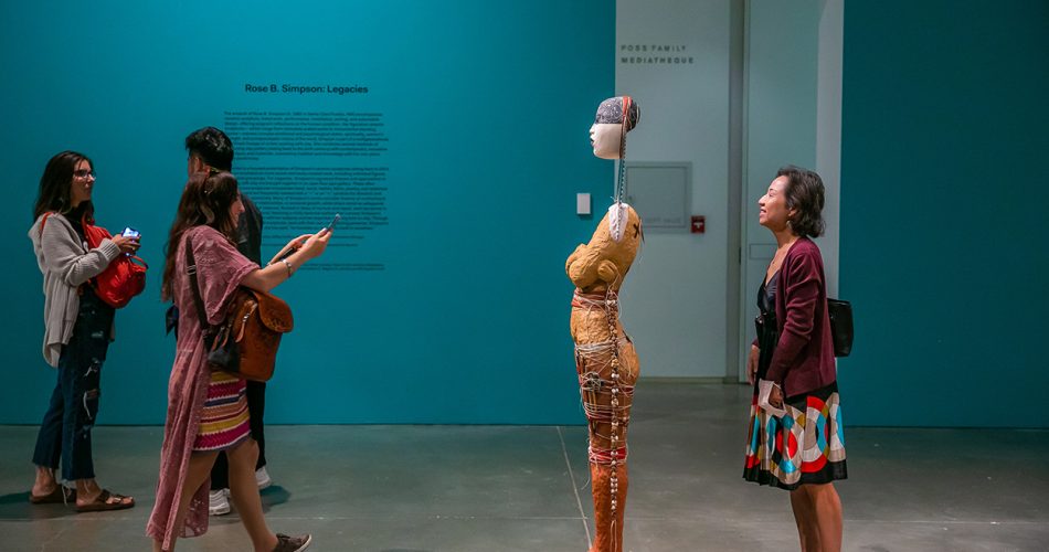 Woman looking out from behind a human-like sculpture while someone takes her picture