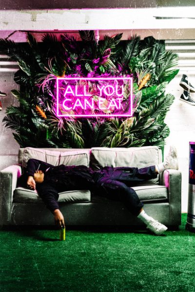 A person laying on a couch under a neon sign reading ALL YOU CAN EAT.