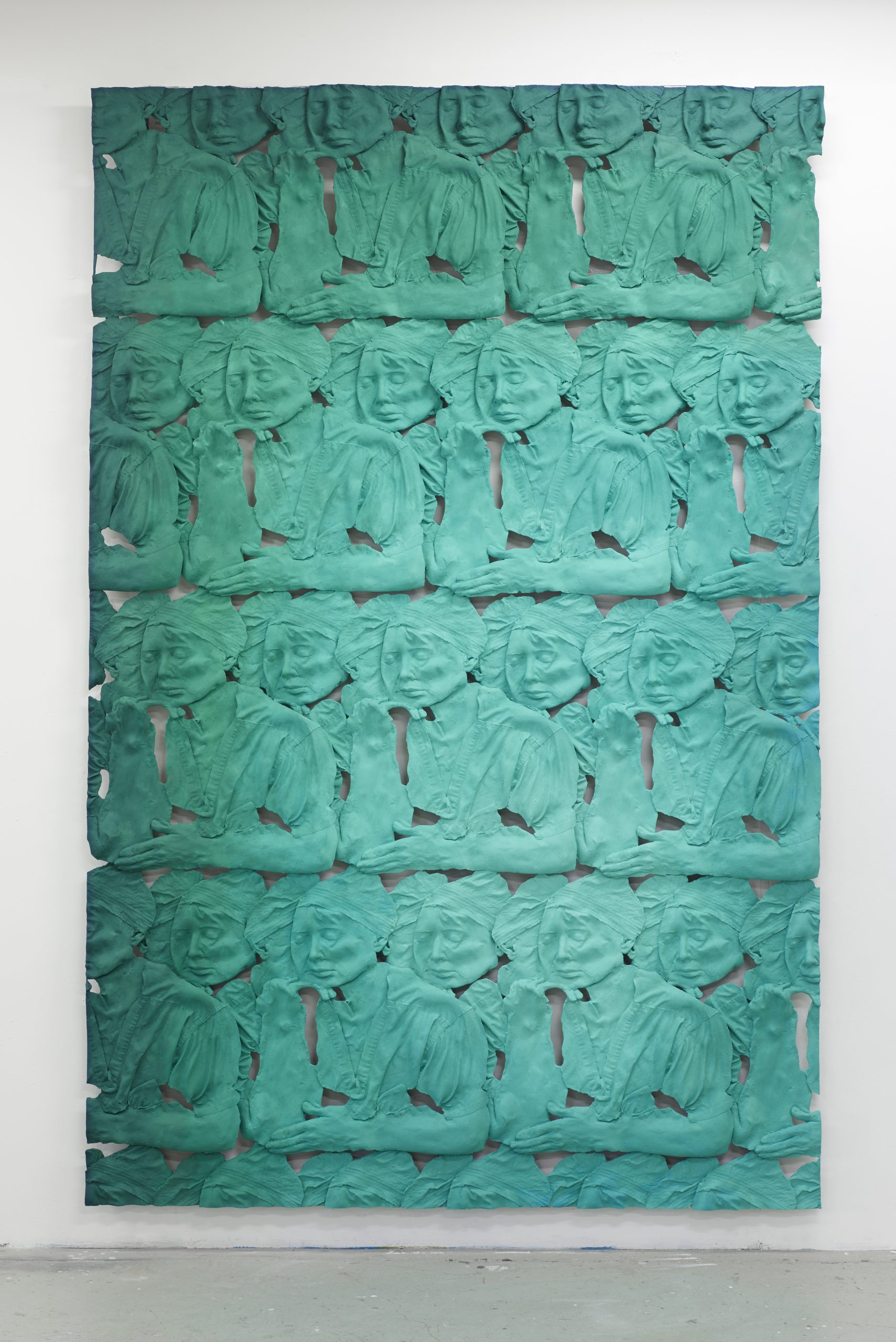A sculpture of several dozen identical green plaster casts of a woman’s head and torso arranged in rows in a rectangular, vertically-oriented architectural frieze.