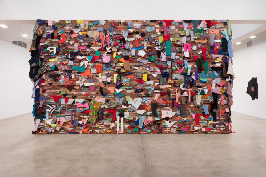 Brick wall installation with colorful clothing sticking out from between the bricks