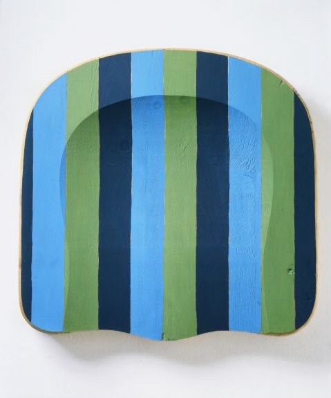 The seat of a wooden chair painted in navy, blue, and green vertical stripes and hung vertically on a wall.
