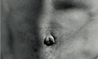 A black-and-white square photograph shows a tight close up of a light-skinned man’s flat, bare stomach with a belly button in the center.