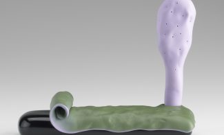 A small ceramic sculpture comprises a shiny black base partially covered by a curling thin green layer and, to the far right, a vertical light purple leaf-like structure.