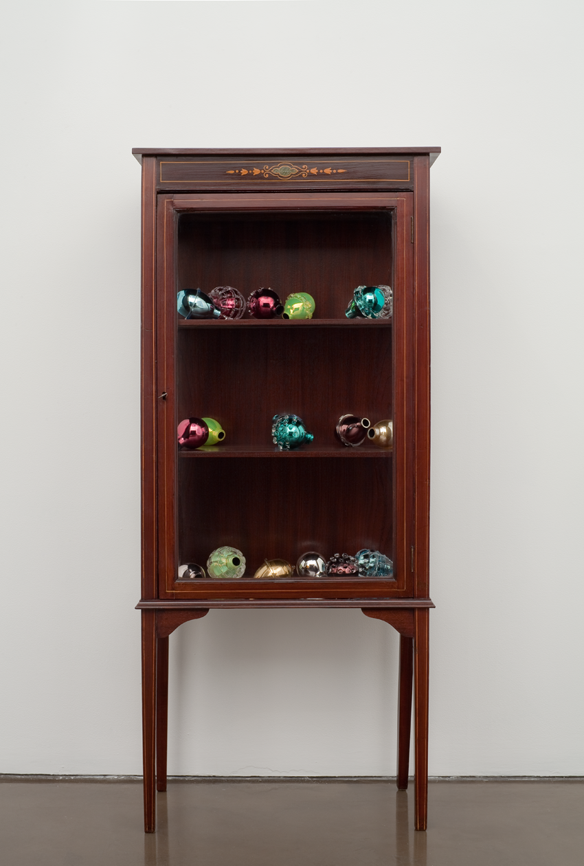 A sculpture comprising an Edwardian wooden cabinet filled with colorful Murano glass grenades that resemble decorative fruit. 