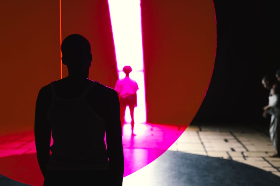 Backlit figures on a stage separated by a red disc of light