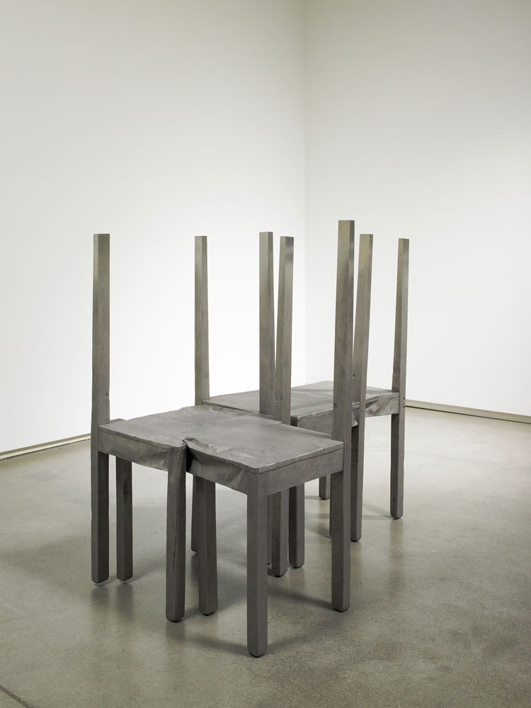 A stainless-steel sculpture of four backless, chairs connected together in the shape of an 