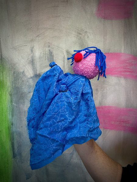 A blue handpuppet with purple face and red nose