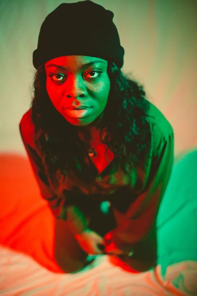 A woman with dark skin and long hair is lit by red and green light from either side