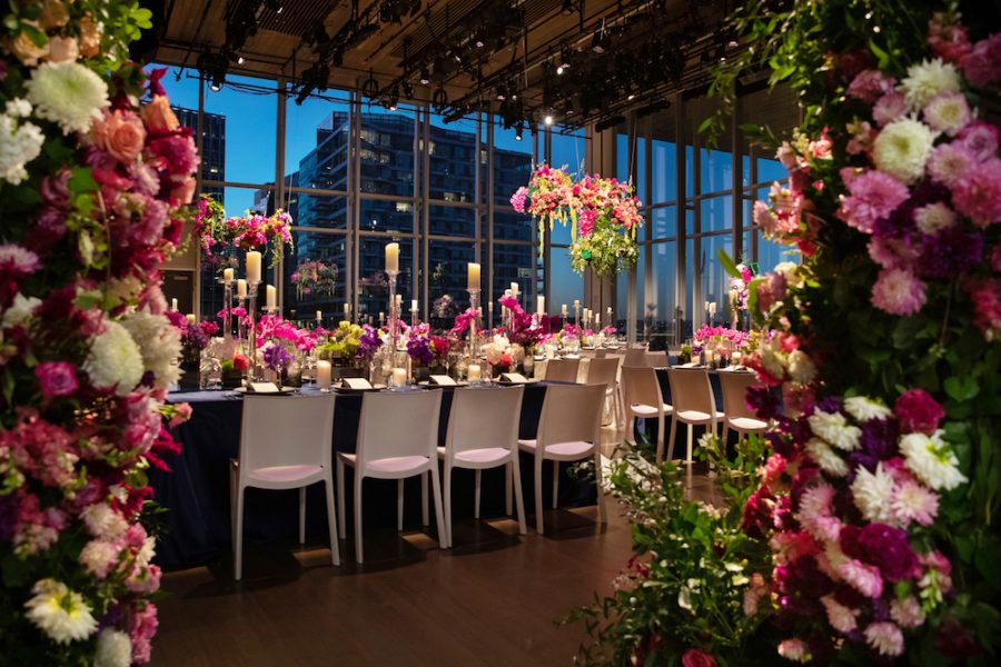 The ICA's theater set for an event with wide window views and hundreds of pink and white flowers.