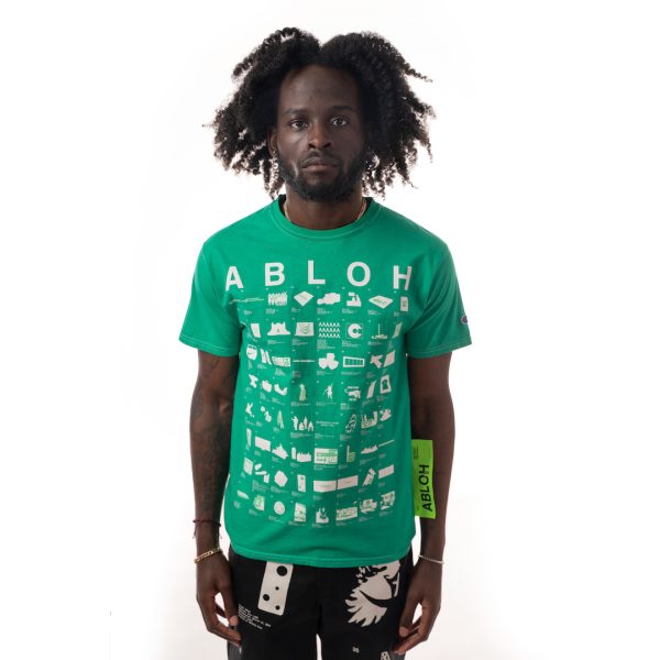 Front view of bright green shirt with rows of artworks in simplified white print and a large yellow-green tag attached to the side, worn by dark skinned model. 