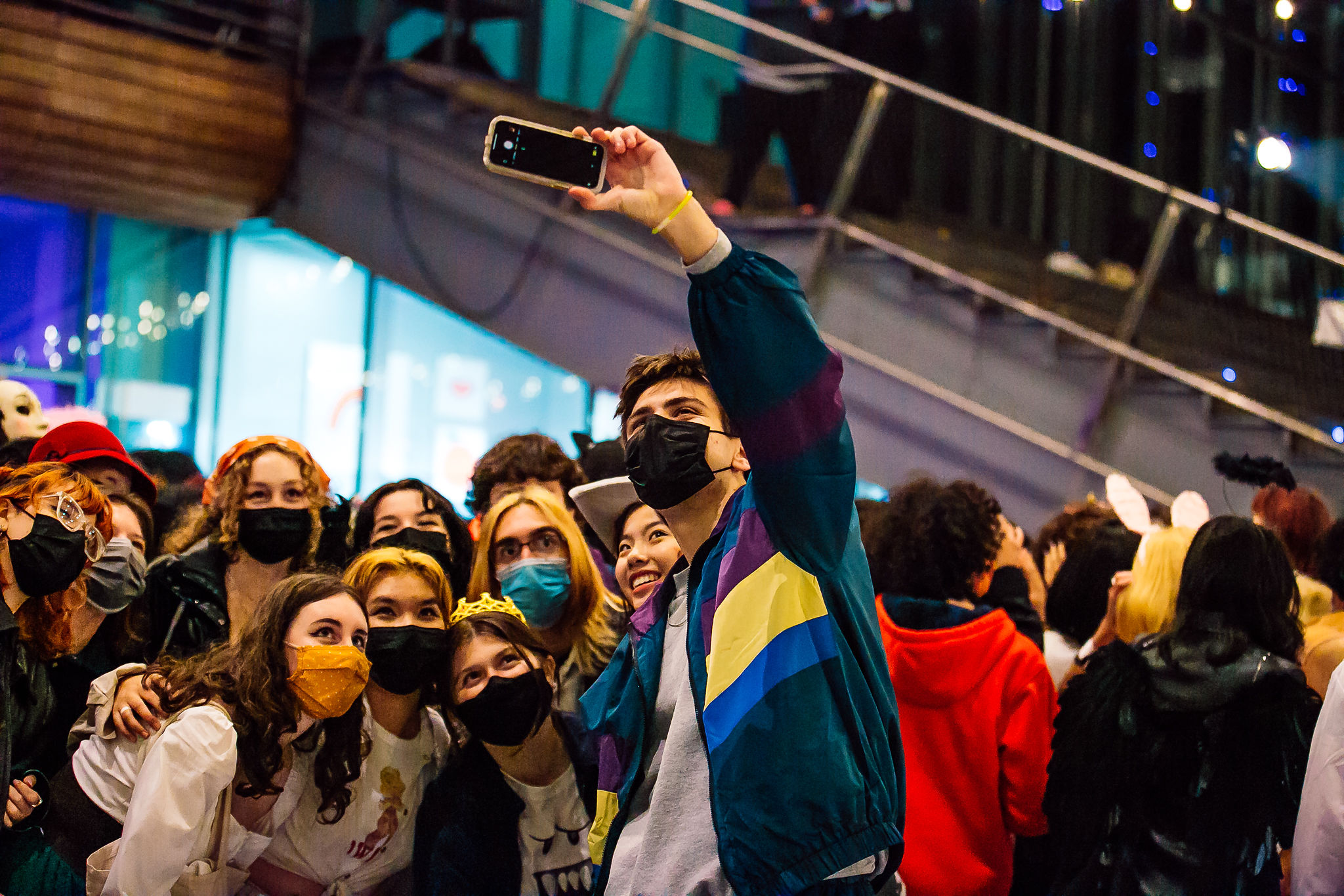A group of teens, mostly wearing face masks, take a selfie in front of the ICA at night