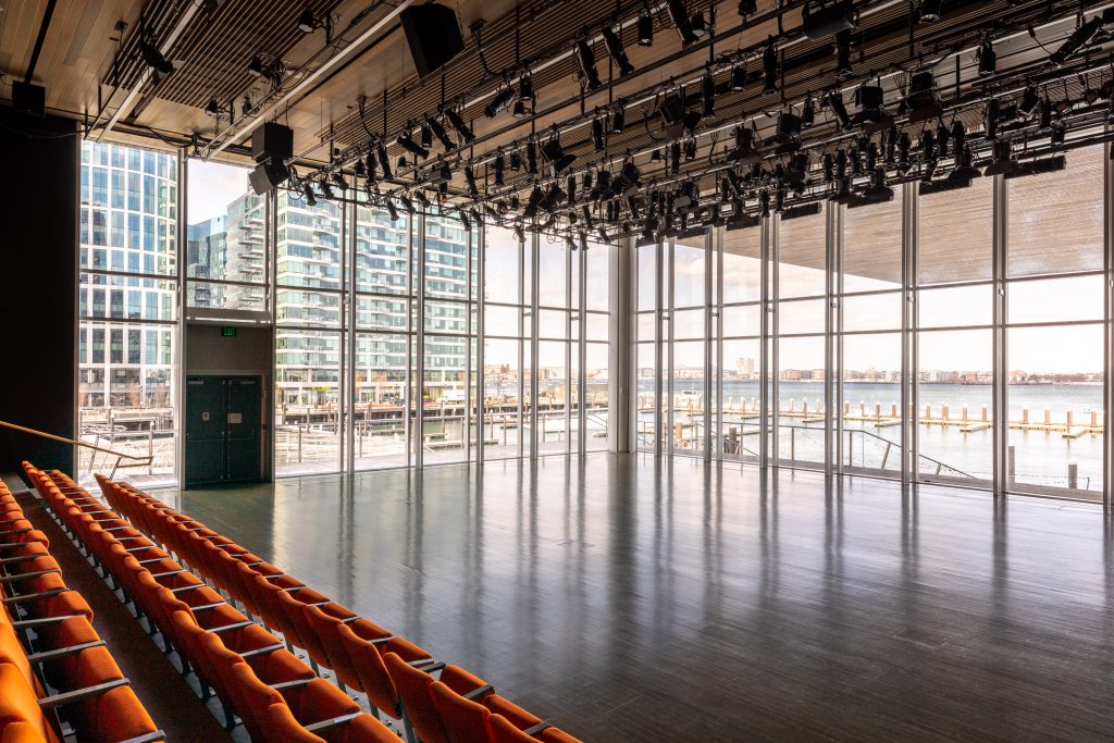 Theater with orange rows of seats and large glass windows overlooking Boston harbor